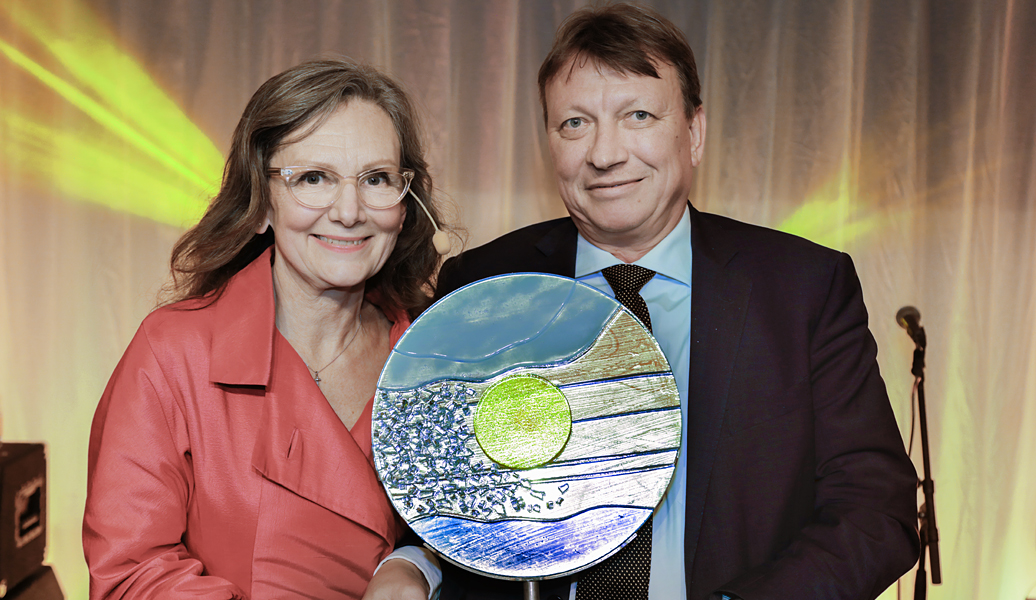 Uma mulher e um homem sorrindo enquanto seguram um prêmio em vidro reciclado.