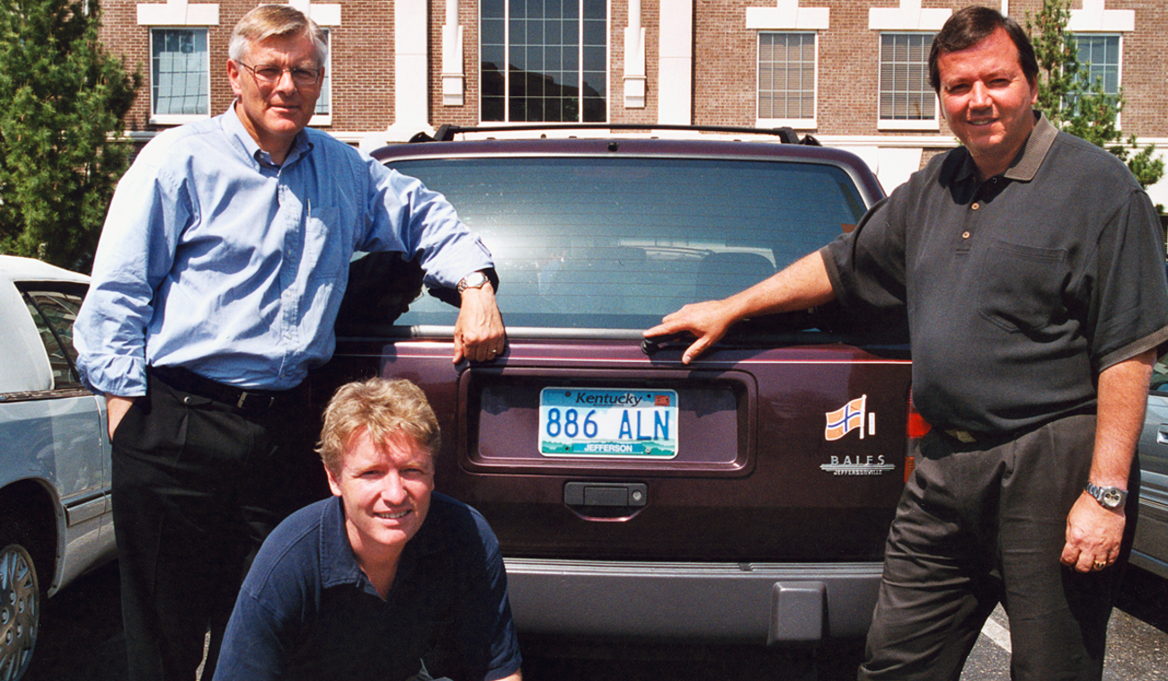 a group of people posing for a photo in front of a car